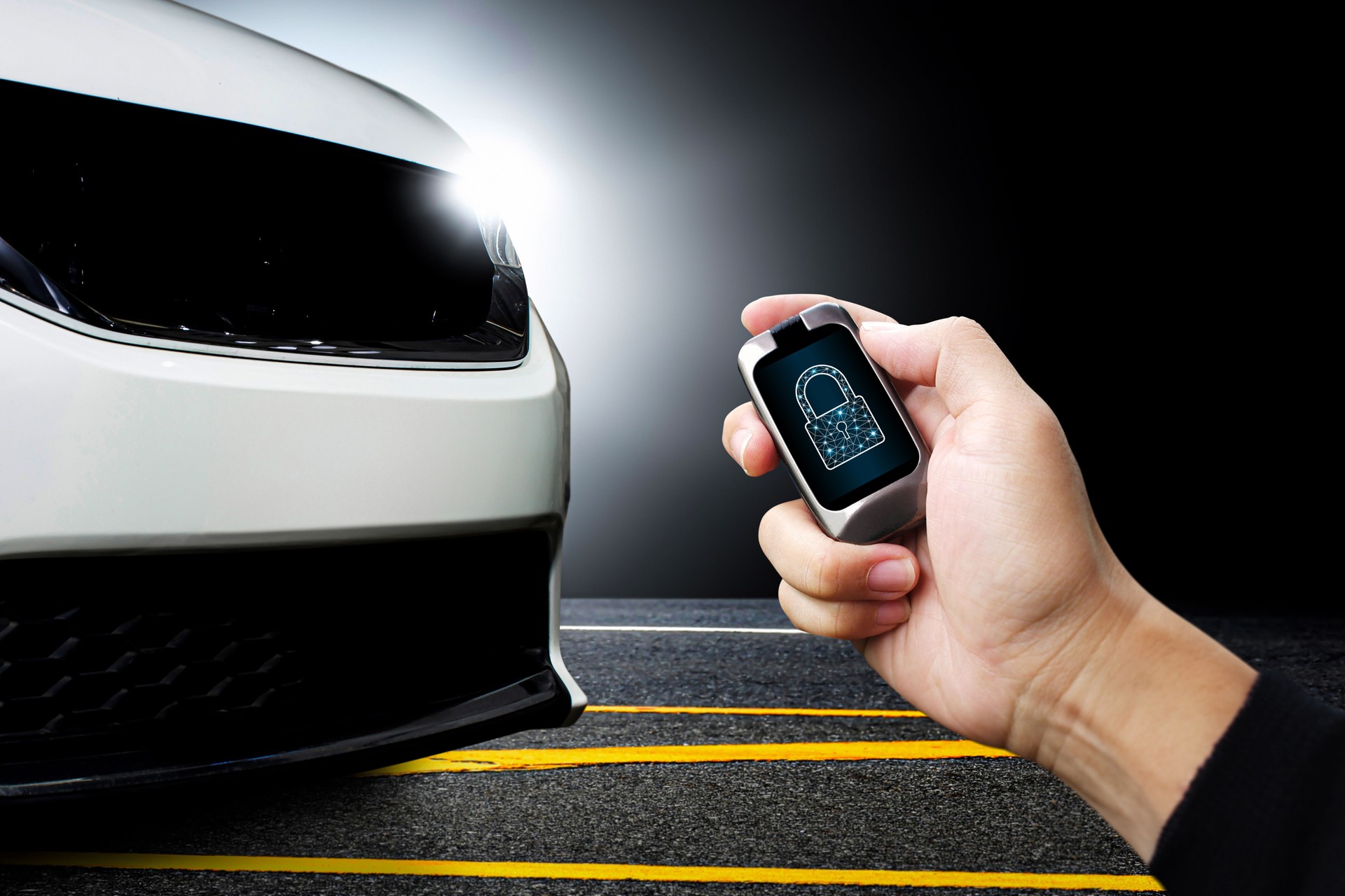 Driver hand holds keyless remote with key locked icon on display with white modern car parked on the road in the background