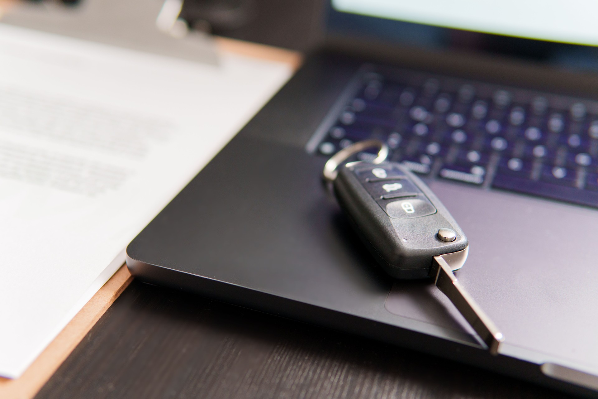 Car keys resting on laptop with sales contract: buying or selling vehicle online